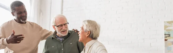 Positivo multiétnico amigos hablando con senior asiático hombre en casa, bandera - foto de stock