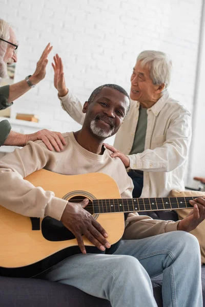 Africano americano homem tocando guitarra acústica perto de amigos inter-raciais em casa — Fotografia de Stock