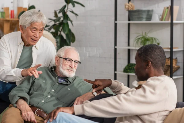 Amis âgés multiculturels parlant sur le canapé à la maison — Photo de stock