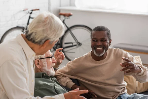 Homem americano africano positivo conversando com amigos seniores na sala de estar — Fotografia de Stock