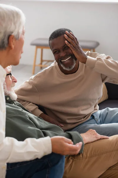 Positivo uomo afroamericano che guarda gli amici multietnici durante la conversazione a casa — Foto stock