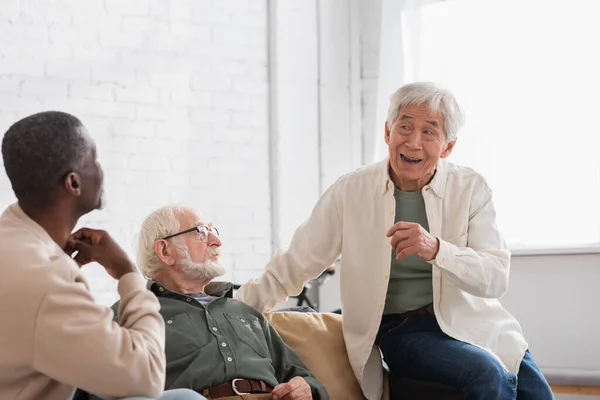 Älterer asiatischer Mann spricht mit multiethnischen Freunden im Wohnzimmer — Stockfoto