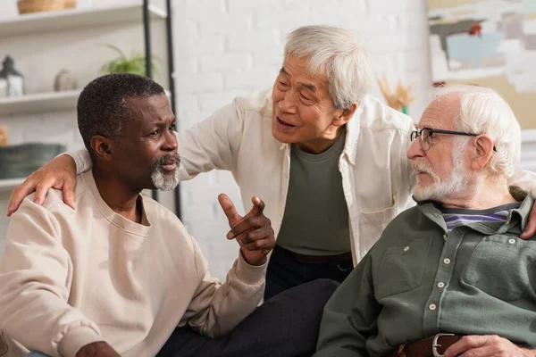 Ancianos amigos interracial hablando en la sala de estar - foto de stock