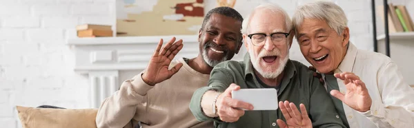 Senior multiethnic friends waving hands during video call on cellphone at home, banner — Stock Photo