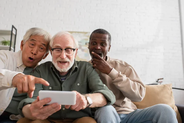 Шокированные межрасовые мужчины смотрят на смартфон рядом с другом дома — стоковое фото