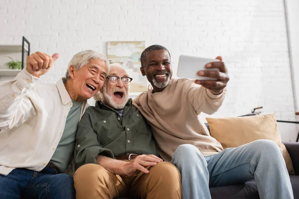 Smiling multiethnic friends using smartphone on couch at home — Stock Photo