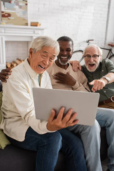 Positive multiethnic senior friends using laptop at home — Stock Photo