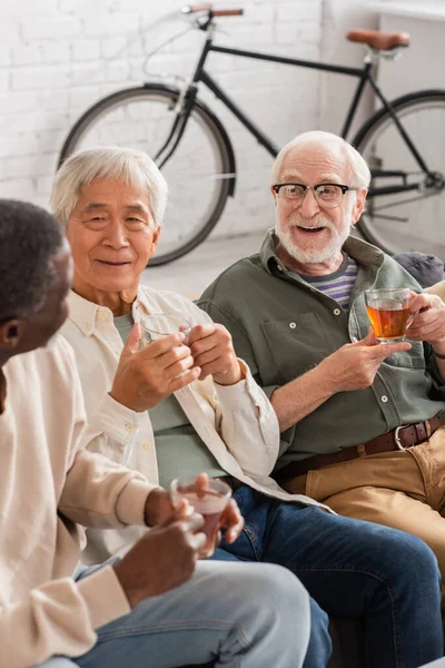 Positive interracial men holding cups of tea at home — Stock Photo