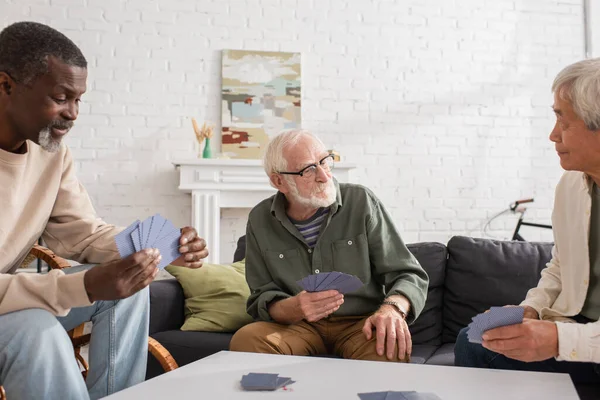 Amigos multiétnicos jugando a las cartas en casa — Stock Photo