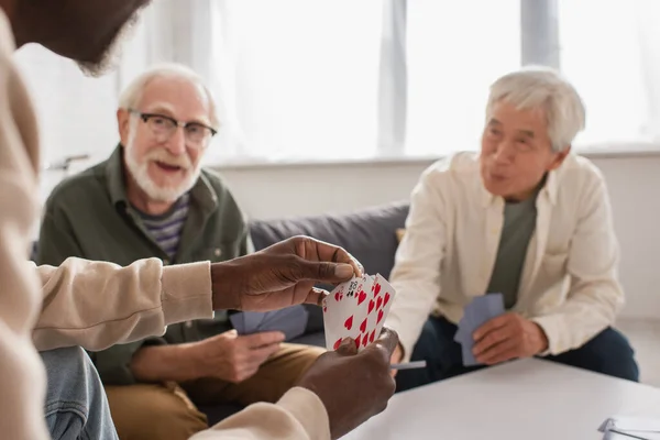 Africano americano homem segurando cartas perto de amigos inter-raciais borrados em casa — Fotografia de Stock