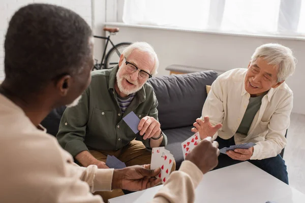 Positive multiethnic senior men playing cards with african american friend at home — Stock Photo