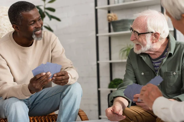 Hombre afroamericano sosteniendo cartas cerca de amigos en casa — Stock Photo