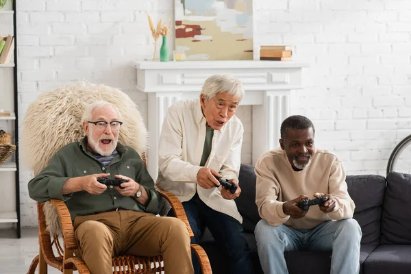 KYIV, UCRANIA - 12 de octubre de 2021: Emocionados amigos interracial jugando videojuegos en casa - foto de stock