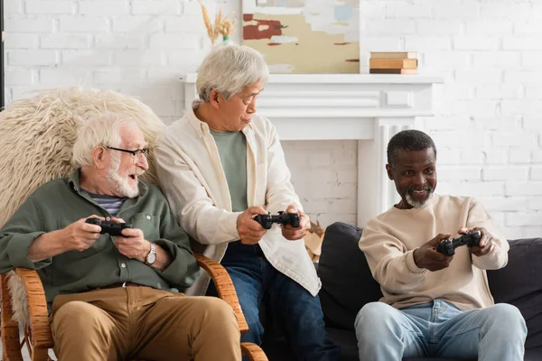 KYIV, UKRAINE - OCTOBER 12, 2021: Smiling african american man playing video game near multiethnic friends at home — Stock Photo