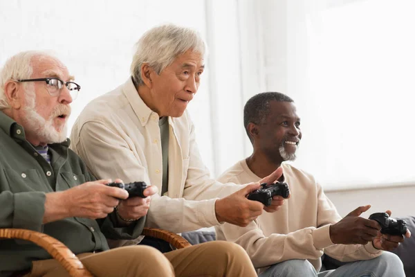 KYIV, UKRAINE - OCTOBER 12, 2021: Focused multiethnic senior men playing video game at home — Stock Photo