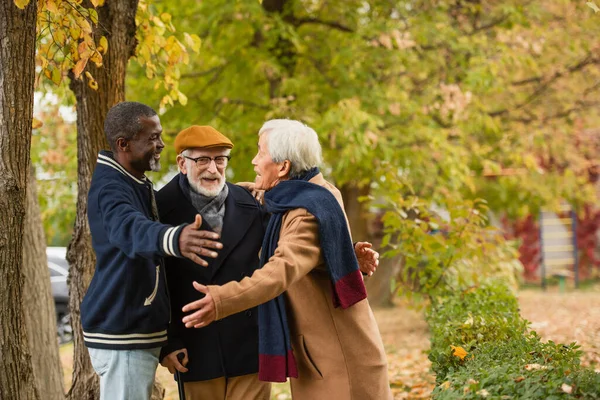 Hombres multiétnicos positivos abrazándose en el parque de otoño - foto de stock