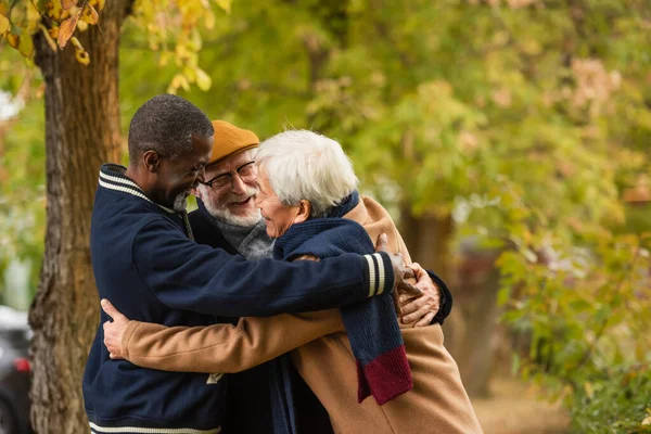 Amici multiculturali positivi che si abbracciano nel parco autunnale — Foto stock