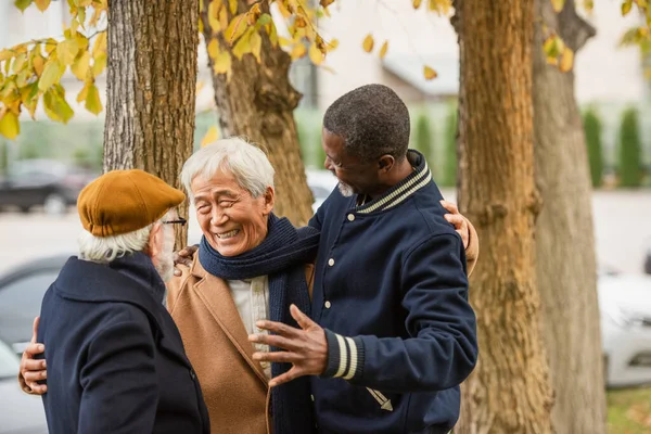 Felice asiatico uomo abbracciare anziani interrazziale amici su urbano strada — Foto stock