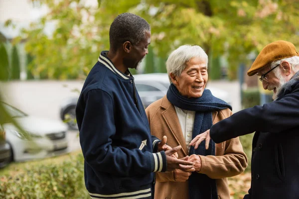 Feliz hombre mayor hablando con amigos multiculturales en el parque de otoño - foto de stock