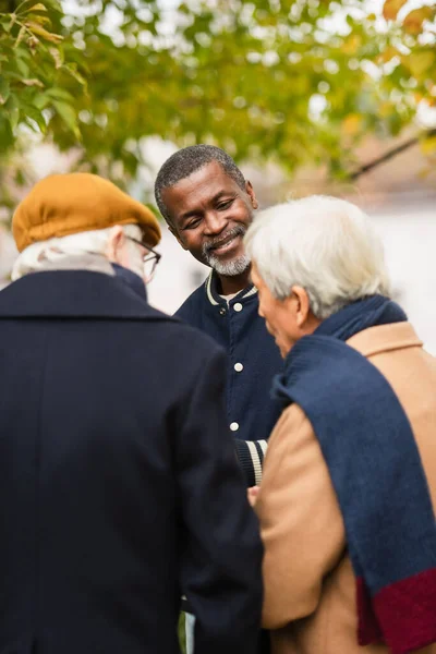 Sonriente hombre afroamericano mirando borrosa amigos multiétnicos en el parque - foto de stock
