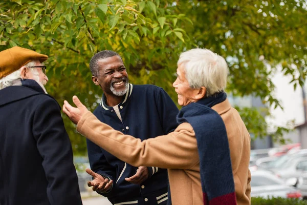 Positive elderly multiethnic friends talking on urban street — Stock Photo