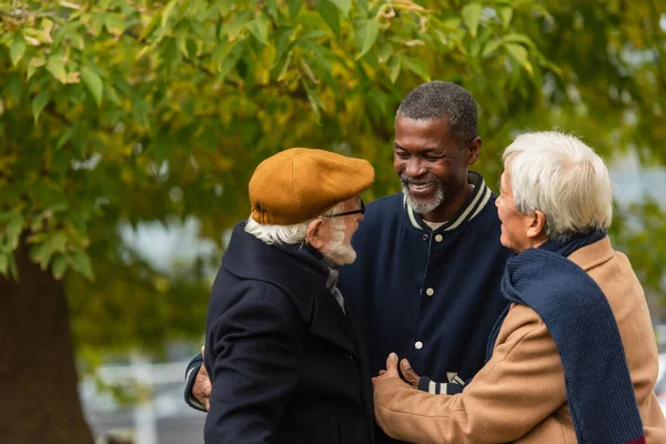 Позитивные многонациональные мужчины обнимаются в осеннем парке — стоковое фото