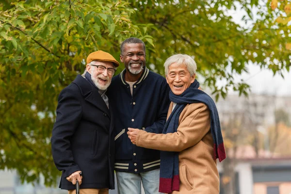 Alegre amigos seniores multiculturais sorrindo para a câmera no parque de outono — Fotografia de Stock