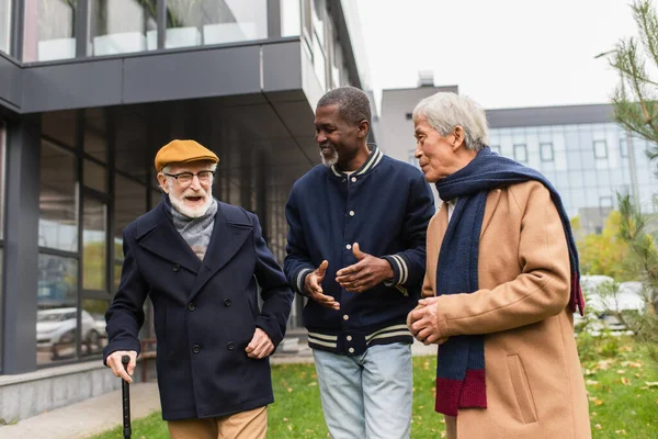 Interracial senior people talking while walking on urban street — Stock Photo