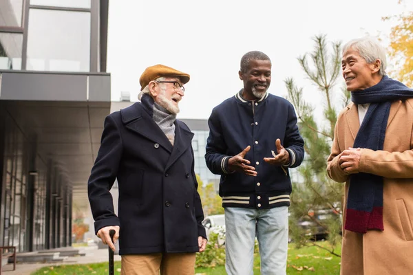 Sonriente hombre afroamericano hablando con amigos interracial en la calle urbana - foto de stock