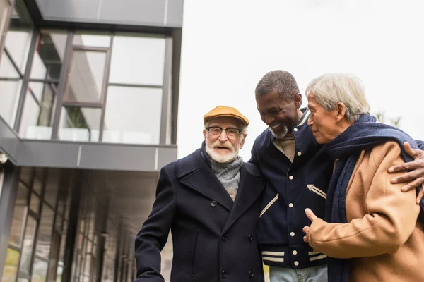 Hombre afroamericano mayor abrazando a amigos multiétnicos en la calle urbana - foto de stock