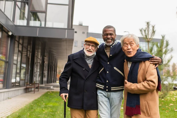 Homme afro-américain étreignant des amis multiethniques joyeux dans la rue urbaine — Photo de stock