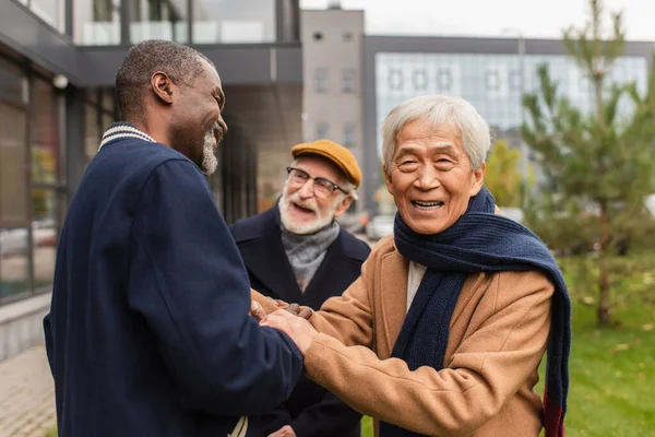 Старший азиат смотрит в камеру рядом с многонациональными друзьями на городской улице — стоковое фото