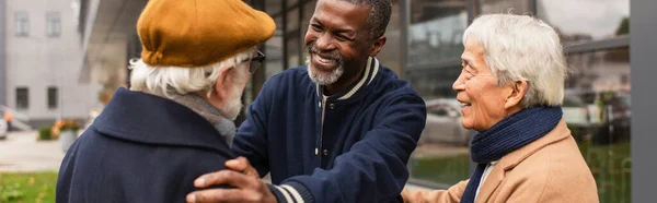 Hombres multiétnicos positivos abrazándose en la calle urbana en otoño, pancarta — Stock Photo