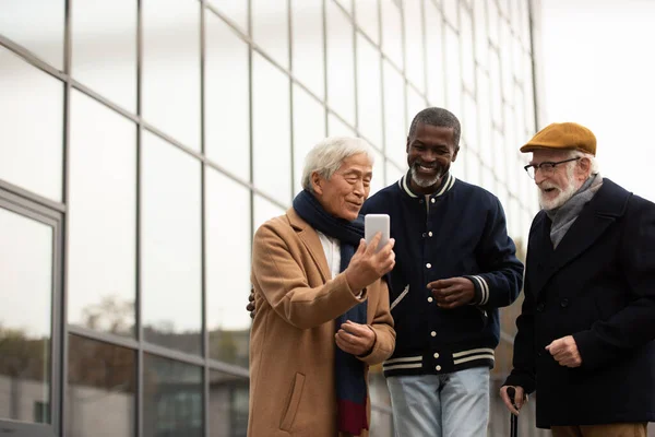 Senior asiatischer Mann benutzt Smartphone in der Nähe von multiethnischen Freunden auf der Stadtstraße — Stockfoto