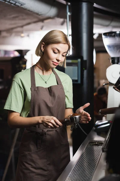 Jovem barista em avental segurando portafilter com café no café — Fotografia de Stock