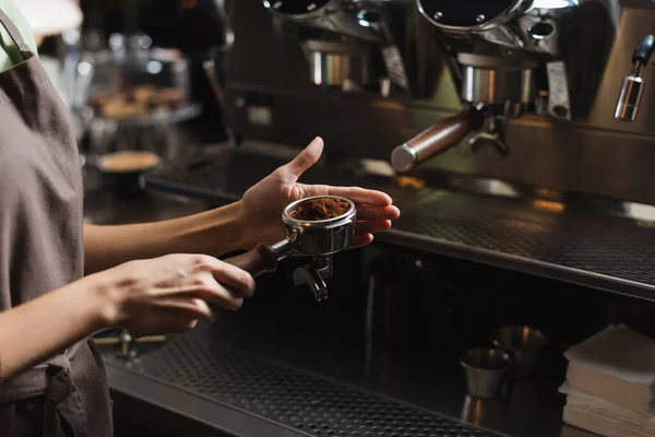 Обрезанный вид на бариста, держащего кофе в портативном фильтре возле размытой кофеварки в кафе — стоковое фото