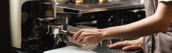 Cropped view of barista holding portafilter near coffee grinder in cafe, banner — Stock Photo