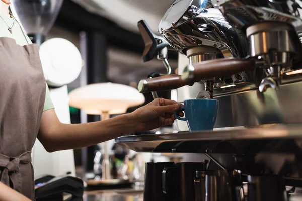 Vista ritagliata del barista che tiene la tazza vicino alla macchina del caffè nel caffè — Foto stock