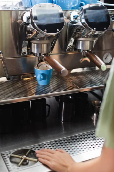 Обрезанный вид на бариста, стоящего возле чашек и кофеварки в кафе — стоковое фото