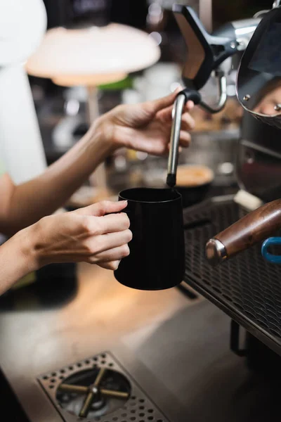 Vue recadrée du barista tenant une cruche à lait près de la baguette à vapeur de la machine à café dans le café — Photo de stock