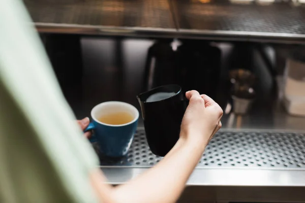 Cropped view of barista holding milk jug and cup in cafe — Stock Photo