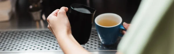 Vue recadrée du barista tenant la cruche de lait et la tasse dans le café, bannière — Photo de stock