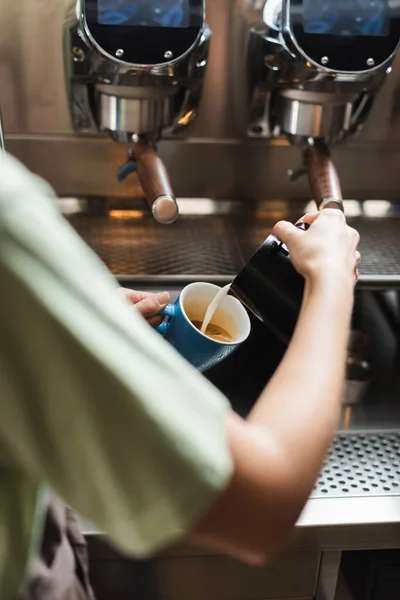 Vista ritagliata di barista versando latte in tazza con caffè vicino macchina da caffè in caffè — Foto stock