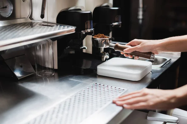 Cropped view of barista holding portafilter near grinder and coffee machine in cafe — Stock Photo