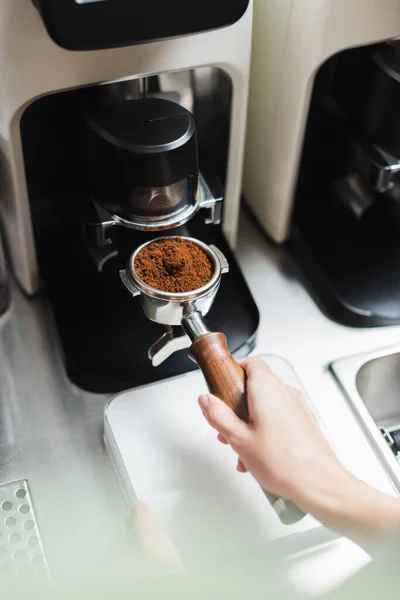 Cropped view of barista holding portafilter of coffee machine near grinder in cafe — Stock Photo