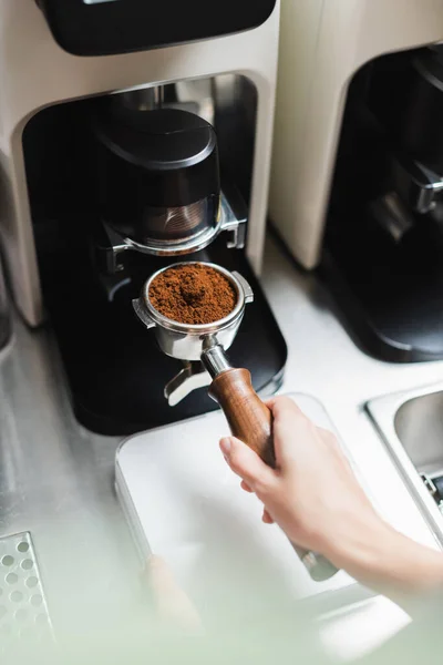 Vista recortada de barista celebración portafilter de la máquina de café cerca de la amoladora en la cafetería - foto de stock