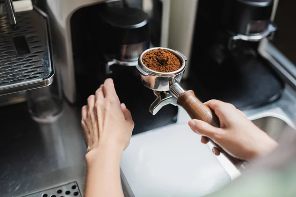 Ausgeschnittene Ansicht des Barista, der einen Filter mit Kaffee in der Nähe der Mühle und Kaffeemaschine im Café hält — Stockfoto