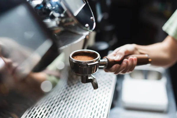 Cropped view of barista holding portafilter with coffee near blurred coffee machine in cafe — Stock Photo