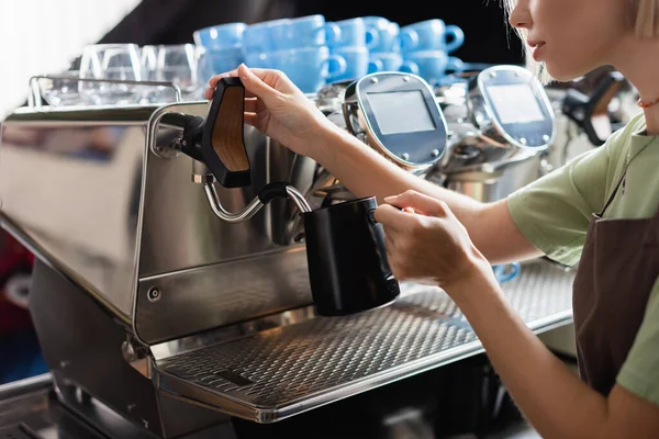 Cropped view of barista holding milk jug near coffee machine with steam wand in cafe — Stock Photo