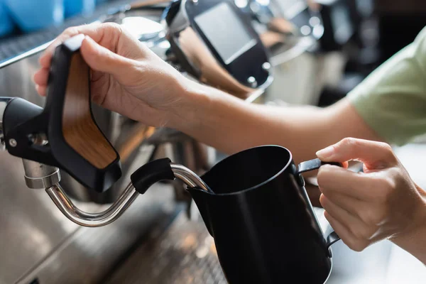 Vista ritagliata del barista che tiene la brocca di latte vicino alla macchina del caffè con la bacchetta del vapore in caffetteria — Foto stock